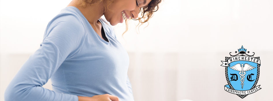 A woman is gently caressing her belly since there is a baby developing.