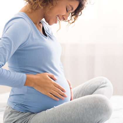 A close up view of a pregnant woman holding her belly, being that a child is developing.
